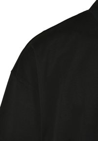 Chemise en coton noir avec une texture lisse, dotée d'un col classique et de manches courtes, affichant un design simple et épuré.