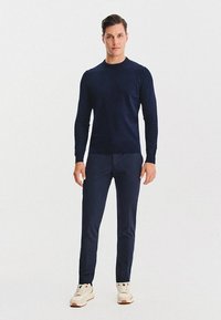 Granatowy sweter z okrągłym dekoltem wykonany z miękkiego materiału, zestawiony z pasującymi tapered spodniami oraz białymi trampkami z wielokolorowymi akcentami.