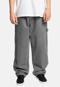 Grå, løse cargobukser med synlige sidelommer, lavet af denim, med synlige sømdetaljer og en afslappet pasform, parret med sorte sneakers.