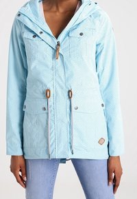 Ljusblå huva jacka med prickigt mönster, justerbara dragsko, framfickor och silverfärgad hårdvara. Mjuk tygtextur.