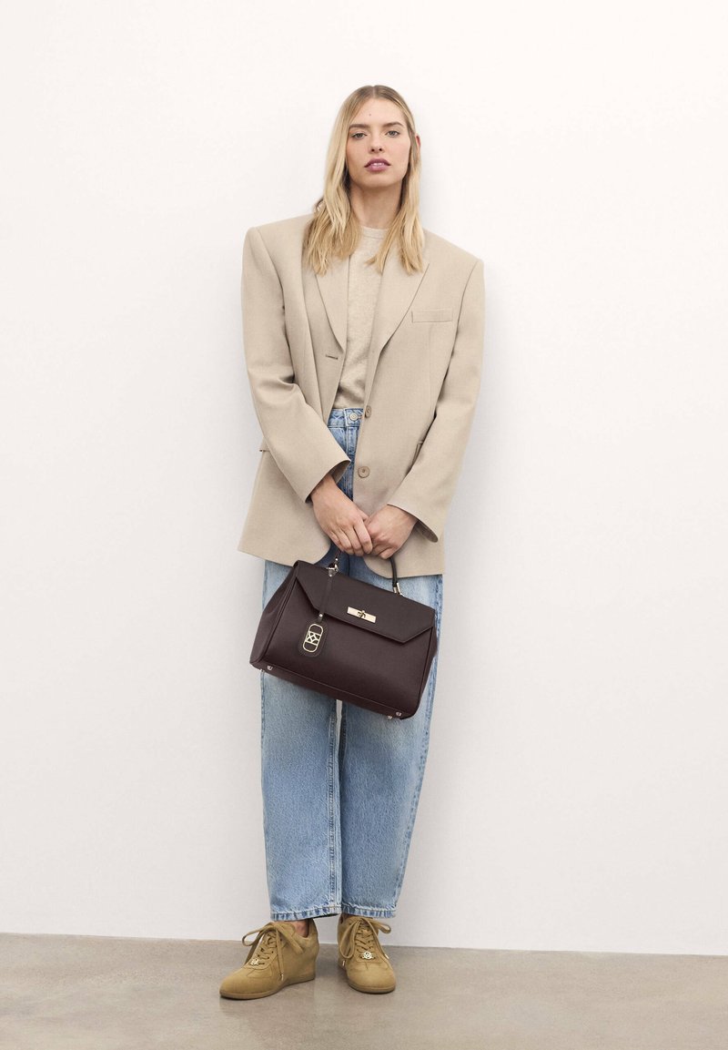 Blazer oversize beige, top grigio chiaro, jeans blu larghi, borsa marrone con hardware dorato e sneakers beige con zeppa su uno sfondo chiaro.