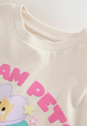 Kreminės spalvos marškinėlių audinys su apvalia iškirpte. Yra rausvos spalvos iškilūs užrašai ir piešinys su animacinio personažo atvaizdu bei žvaigždutėmis.