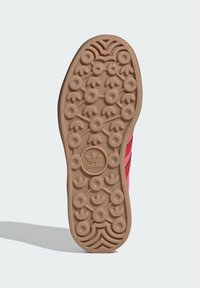 Sola de ténis Adidas em borracha castanha clara, com padrões de tração circulares e um logótipo central. Superfície texturizada com acentos arredondados.