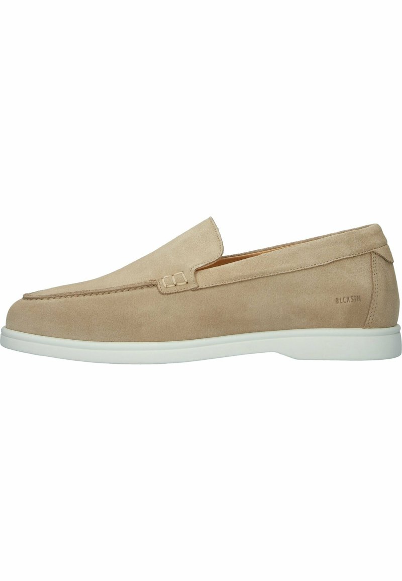 Mocassin beige en daim à enfiler avec semelle en caoutchouc blanche et coutures minimalistes, présentant un détail de marque près du talon.