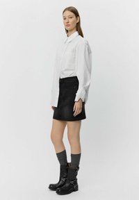 White collared shirt, black denim skirt, gray knee-high socks, black ankle boots. Skirt features subtle texture and a front button closure.