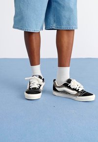 Sorte og hvide sneakers med leopardmønster, der har hvide snørebånd, et lavtopdesign og en blanding af teksturerede materialer.