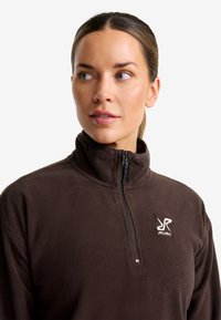 Brauner Fleece-Pullover mit hohem Kragen, halblangem Reißverschluss vorne und weißem Logo auf der Brust. Weicher Stoff und lässige Passform.