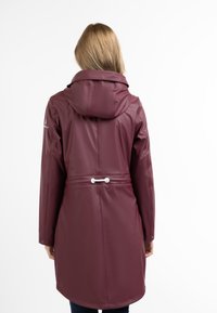 Pardoseală de ploaie de culoare vinie cu glugă, având o talie ajustată, design fără cusături, șnur elastic și accente hardware albe.