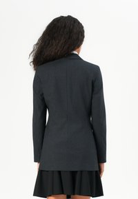 Tmavě šedý oblekový sako s jemným proužkem, dlouhými rukávy, slim fit střihem a mírně zakřiveným lemem, spárované s černou plisovanou sukní.
