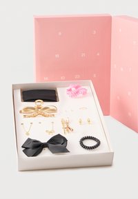 Σετ κοσμημάτων σε μπεζ κουτί με ροζ καπάκι. Περιλαμβάνει χρυσά κλιπ, μαύρο φιόγκο από κορδέλα, σκουλαρίκια, ροζ λαστιχάκι μαλλιών και βραχιόλι με χάντρες.
