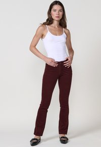 Bordeaux corduroy jeans met een aansluitend ontwerp en een lichte flare aan de onderkant, gecombineerd met een witte spaghetti strap top en zwarte platte schoenen.