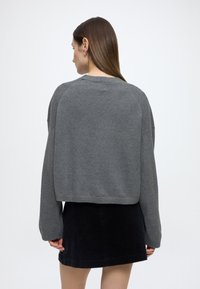 Sivý krátky sveter s dlhými rukávmi, mäkkou textúrou a rebrovaným lemom, doplnený o čiernu kordurovú sukňu. Jednoduchý dizajn bez vzorov.