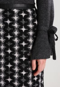 Maglione grigio texturizzato con maniche a campana, abbinato a una gonna a fantasia bianco e nero con forme di stelle e linee ondulate.