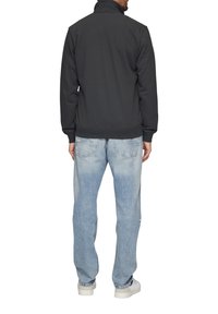 Sudadera gris con cremallera y cuello alto, acompañada de vaqueros claros ajustados y zapatillas blancas, vista desde la espalda. Ajuste casual y textura suave.