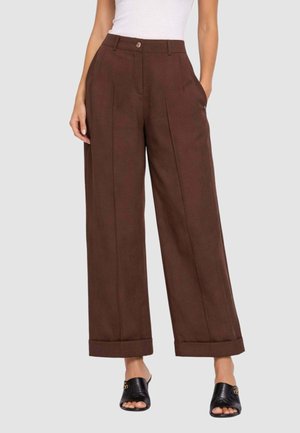 Donna che indossa pantaloni marroni a gamba larga e vita alta con risvolti, top bianco senza maniche e mule nere con punta aperta.