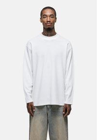 White long-sleeve shirt with a textured fabric, round neckline, and relaxed fit, paired with faded, loose denim jeans.