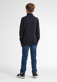 Navy Pullover mit hohem Kragen, langen Ärmeln und geripptem Saum, kombiniert mit blauen Jeans und schwarzen Sneakers. Einfaches, schlichtes Design.