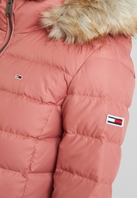 Pink puffer jacket with a fur-trimmed hood, quilted texture, and a small branded logo on the sleeve. Soft, lightweight material.