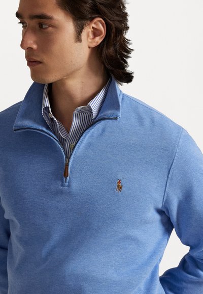 Sweater azul-claro com meia-zips, feito de tecido de malha texturizada, apresentando um pequeno logotipo bordado no lado esquerdo do peito e uma camisa com colarinho em contraste por baixo.