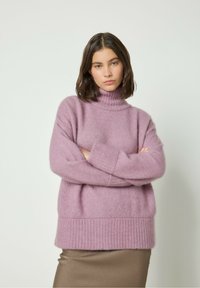 Mėtinės spalvos turtleneck megztinis iš minkštos, pūkuotos medžiagos su plačia susiūta apatine dalimi ir rankovėmis. Suderintas su lygiu ruduo sijonu.