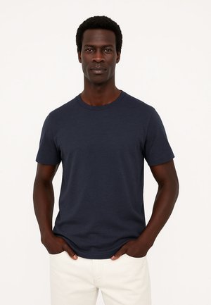 T-shirt in cotone blu navy con collo rotondo, maniche corte e texture liscia, indossato con pantaloni chiari. Nessun motivo o dettaglio.