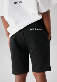 Svarta bomullsshorts med elastisk midja och en bakficka. "ALLSAINTS" är tryckt i vitt på midjan och fickan.