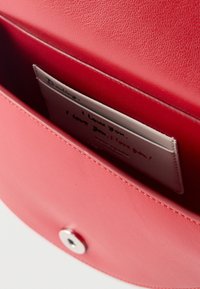 Κόκκινο δερμάτινο πορτοφόλι ανοιχτό που αποκαλύπτει μια κάρτα με επαναλαμβανόμενο χειρόγραφο μήνυμα «Σ' αγαπώ» μέσα σε μια μικρή τσέπη.