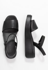 Sandali platform in pelle nera caratterizzati da un design a fascia larga, cinturino alla caviglia regolabile e superficie liscia.