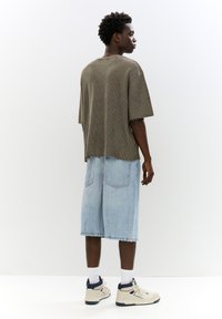 Oliven grøn ribbet oversized t-shirt parret med lyseblå denimshorts, båret med hvide strømper og beige sneakers. Enkelt design og afslappet pasform.