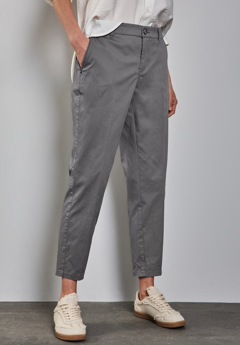 Grå chinos med avspänt snitt, som har sidofickor, knäppning med knapp, uppvikta muddar och sliten textur, kombinerat med beiga sneakers.