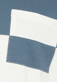 Gros plan d’un tissu à larges rayures horizontales alternant bleu et blanc, montrant des coutures détaillées le long des bords.