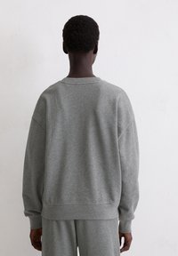 Szary oversize'owy sweatshirt z miękkiego materiału, z okrągłym dekoltem, opadającymi ramionami oraz ściągaczami na rękawach. Czysty design bez widocznych logo.