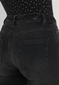 Black denim jeans featuring a high waist, back pockets, and a leather brand label. The fabric has a smooth texture with a slight stretch.