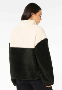 Wollig, farbblockierter Pullover in Creme und Dunkelgrün. Hoher Kragen, lockere Passform und weiche Textur mit kontrastierendem Paneeldesign.