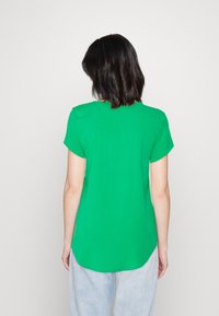 Grünes T-Shirt mit kurzen Ärmeln, rundem Ausschnitt, glattem Stoff und abgerundetem Saum. Kombiniert mit hellblauen, locker sitzenden Jeans.