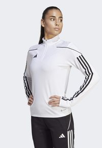 Weißes Sportoberteil mit langen Ärmeln und einem Viertelreißverschluss, ausgestattet mit schwarzen horizontalen Streifen an den Ärmeln und dem Adidas-Logo auf der Brust.