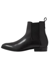 Botte Chelsea en cuir noir avec panneaux latéraux élastiques, bout arrondi et petit talon empilé. Texture lisse et design épuré.