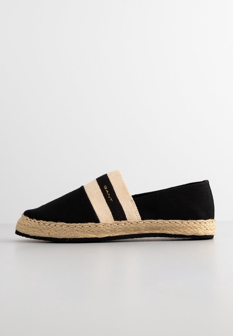 Chaussure espadrille noire avec une tige en toile, dotée de sangles élastiques beiges et d'une semelle en corde de jute. Design minimaliste avec un détail de logo.