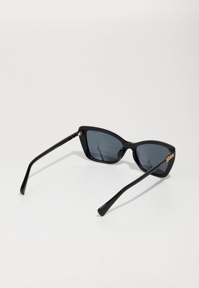 Gafas de sol de ojo de gato negras con lentes oscuros, marco de plástico brillante y acentos de hardware en tono dorado en las patillas.