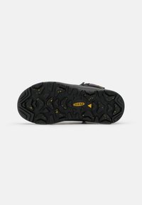 Suela de zapato de goma negra con patrones de tracción profundos y dentados; presenta detalles en amarillo para mejorar el agarre y la tracción.
