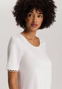 Camiseta blanca de manga corta con cuello redondeado y borde festoneado en las mangas. Hecha de una tela suave, ofrece un ajuste relajado.