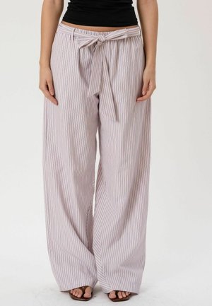 Femme portant un pantalon taille haute à jambes larges avec des rayures verticales claires et foncées, ceinture nouée à la taille, et des sandales marron.
