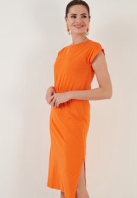 Orangenes Baumwollkleid mit kurzen Ärmeln, das einen lockeren Schnitt, einen seitlichen Schlitz und einen runden Ausschnitt aufweist. Glatte Textur, lässiges Design.