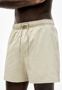 Beige Badehosen mit strukturiertem Oberflächen, elastischem Bund und Kordelzug. Enthält seitliche Taschen und ein lockeres Fit-Design.