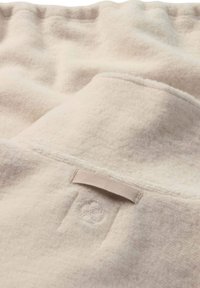 Cremfarbener Fleece-Decke mit weicher Textur, ausgestattet mit einem kleinen Stoffetikett und subtiler Markenkennzeichnung, die in das Material eingestickt ist.