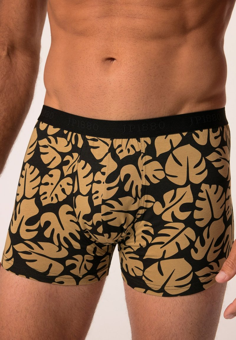 Černé boxerky s tropickým vzorem listů ve zlaté barvě, vyrobené z měkké látky s elastickým černým pasem, na kterém je vytištěné jméno značky.