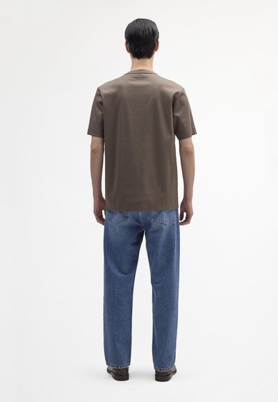 Bruine short-sleeve shirt gecombineerd met losse blauwe denim jeans; het shirt heeft een rechte snit en een zachte textuur, de jeans zijn vervaagd met achterzakken.