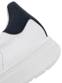 Bílá texturovaná pata tenisky s tlustou podrážkou a černým polstrovaným límcem na bílém pozadí.