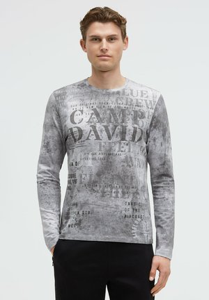 Langärmliges graues T-Shirt aus strukturiertem Stoff mit bedrucktem Text in verschiedenen Schriftarten und -größen, mit Rundhalsausschnitt und figurbetonter Passform.