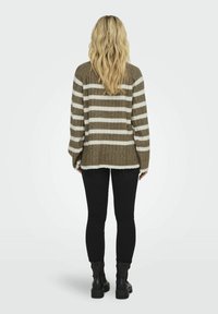 Raidallinen villapaita ruskeassa ja kermanvärisessä, jossa on ribbitekstuuri, löysä istuvuus ja pitkät hihat. Yhdistetty mustiin legginsseihin ja saappaisiin.